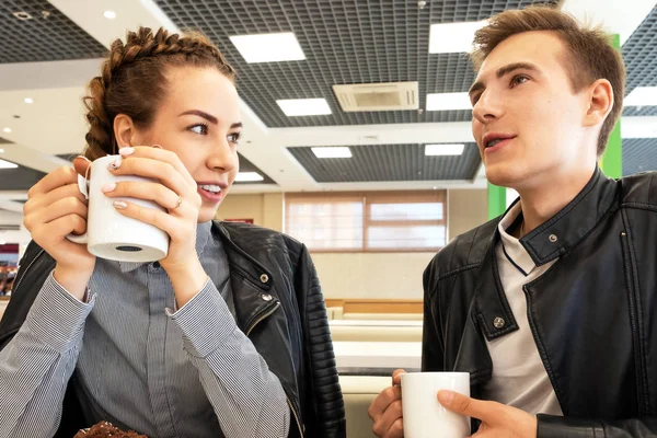 Genç çift el, gülümsüyor ve görüşmeler Kupalar ile kafede oturur