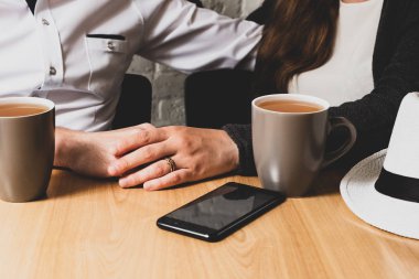 Bir masada erkek ele oturuyor ve yukarıdan bu bir el tarafından okşadı. El bir erkek El okşadı. Bir tablo üzerinde telefon yalan ve bir fincan çay değil. Fotoğraf renkli.
