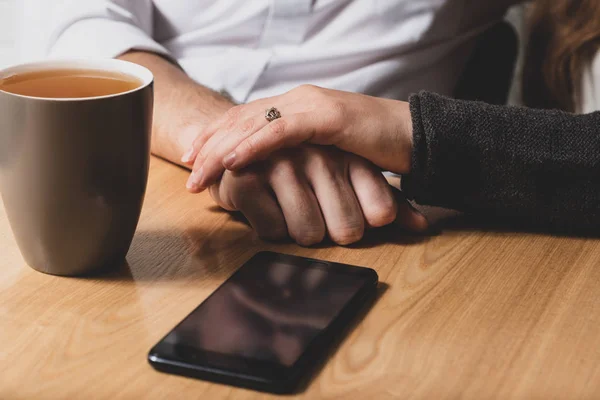 Bir masada erkek ele oturuyor ve yukarıdan bu bir el tarafından okşadı. El bir erkek El okşadı. Bir tablo üzerinde telefon yalan ve bir fincan çay değil. Fotoğraf renkli.