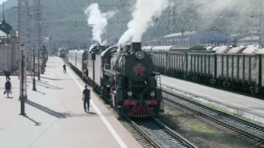 Slyudyanka, Irkutsk region, Rusya Federasyonu - 18 Ağustos 2018: eski Turizm lokomotif maliyeti tren istasyonunda. Bir borudan sigaran yoktur ve Tekerlekli çiftler altından. Turistler peron göre gidin ve fotoğraflandı.