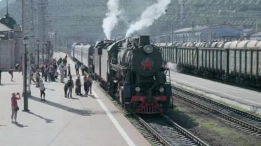 Slyudyanka, Irkutsk region, Rusya Federasyonu - 18 Ağustos 2018: eski Turizm lokomotif maliyeti tren istasyonunda. Bir borudan sigaran yoktur ve Tekerlekli çiftler altından. Turistler peron göre gidin ve fotoğraflandı.
