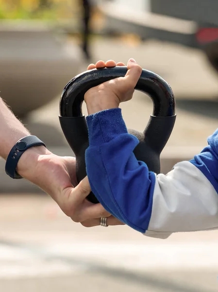 An adult's hand helps a child lift a weight. The hand of an adult helps the child's hand to lift the weight.