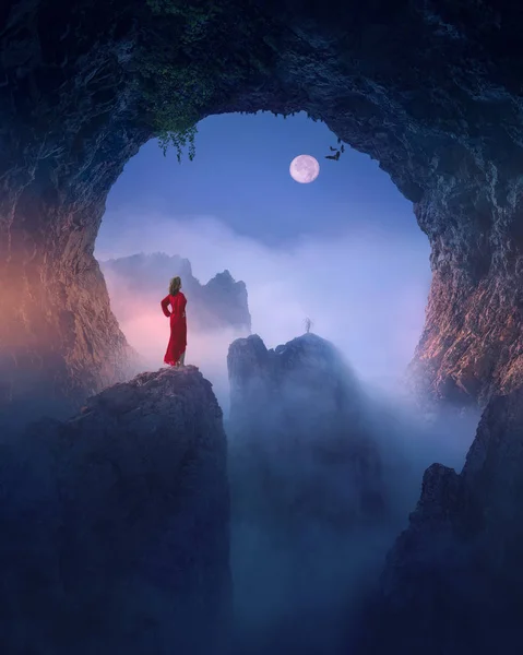 Mujer vestida de rojo contra la luna en espeluznante cueva — Foto de Stock