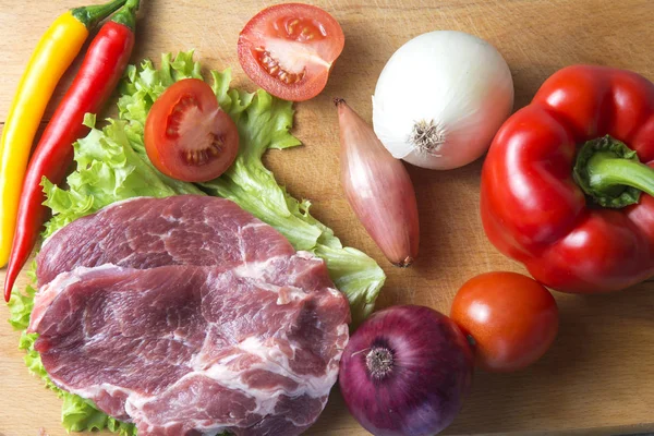 Domuz eti boyun eti biftek marul, turp, domates, kırmızı biber, sarı biber, yeşil kırmızı biber, sarı biber, kırmızı biber, kara biber ve arka plan üzerinde üzerinde. Yatay. Kırmızı soğan, arpacık. Mermer et