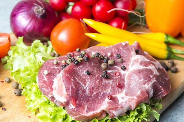 Domuz eti boyun eti biftek marul, turp, domates, kırmızı biber, sarı biber, yeşil kırmızı biber, sarı biber, kırmızı biber, kara biber ve arka plan üzerinde üzerinde. Yatay. Kırmızı soğan, arpacık. Mermer et