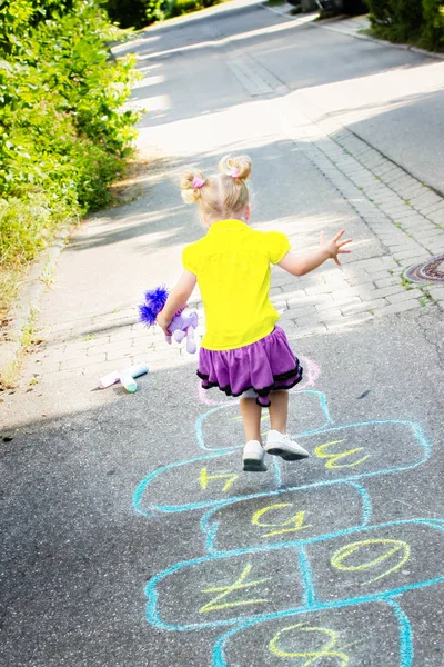 Blondes Kleines Mädchen Mit Spielzeug Der Hand Spielt Hopscotch Auf — Stockfoto