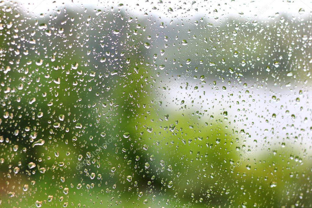 Raindrops on the glass. A blurred view of the lake surrounded by green trees in the background.