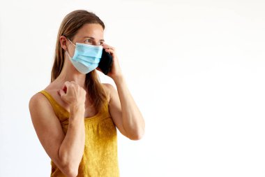 Tıbbi maskeli bir kadın cep telefonuyla konuşuyor.