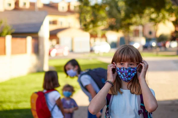 Yüz maskeli bir çocuk, karantinadan sonra okula geri dönüyor. Sarışın kız maskesini takıyor.