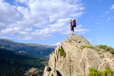 Sırt çantalı bir kadın dağın tepesinde duruyor..
