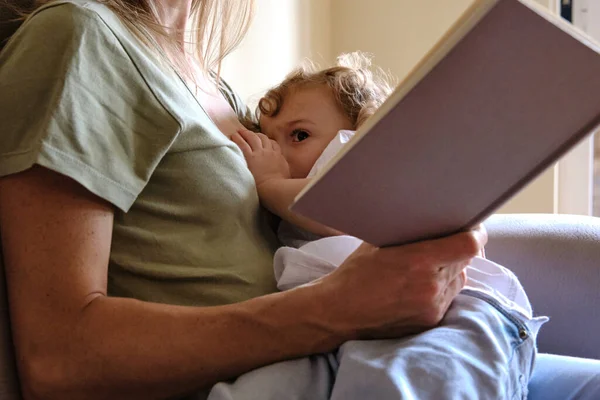 Anne rahat bir kitap okurken çocuğunu emziriyor..