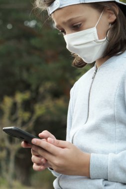 Dışarıda elinde cep telefonu tutan bir maske takan genç bir adam..