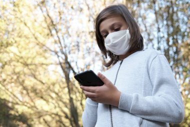 Koruyucu maskeli genç cep telefonuyla sohbet ediyor, seçici odaklı.