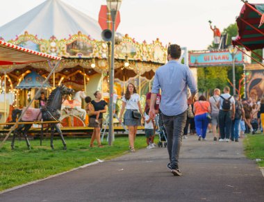 Bir adam Sint Rosa festivalinin çıkışına doğru yürüyor. Konumlar ve diğer ziyaretçiler onun etrafında görülebilir.