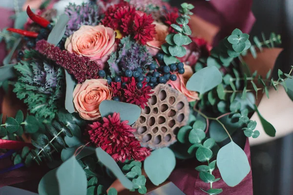 Bouquet of flowers in red, burgundy and shades of Marsala. Ingredients: protea, roses, berries, eucalyptus, cotton flower, lotus flower, chrysanthemum, ornamental cabbage. Flower composition.