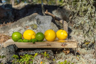 Yaz içecekleri. İskandinav doğasının arka planında bir bardak su, limon, limon ve nane. Farklı su damlaları kombinasyonları. İsveç