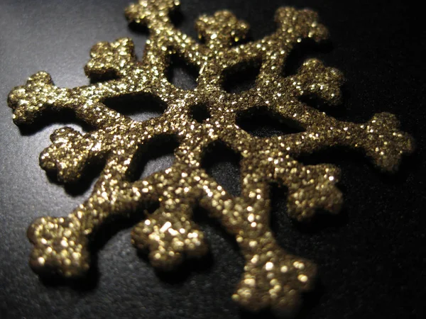 Metal snowflake with gold sequins on black background. Gold snowflake with glitter and shimmer. Christmas decorative element, toy. Selective focus, macro, close-up.