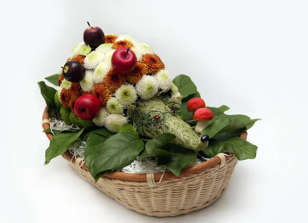 Bouquet of flowers in the form of a hedgehog in a basket on a white background. Floral composition. Flower hedgehog of white and orange chrysanthemums with glasses, mushrooms and apples.