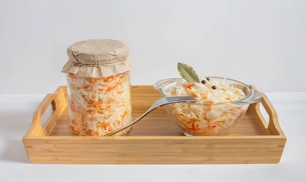 Homemade sauerkraut. Fermented food. Sauerkraut with carrots in a glass jar and bowl in a wooden tray on a white background