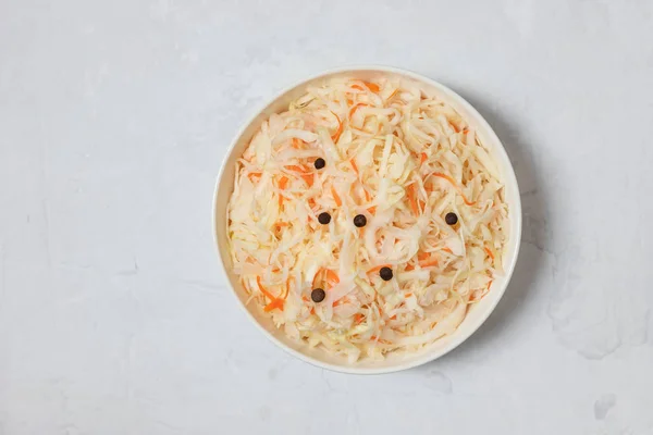 Homemade sauerkraut. Fermented food. Sauerkraut with carrots in a bowl on a concrete white background.