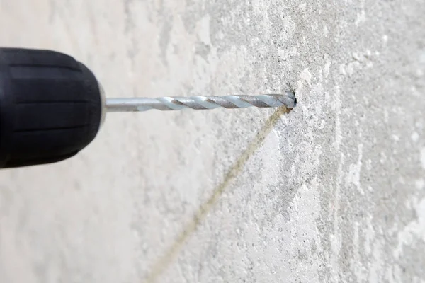 construction work, electric drill drills a hole in the wall, close-up