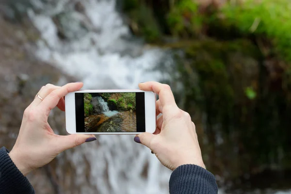 Mãos femininas com um telefone tirar uma foto de uma cachoeira, close-u — Fotografia de Stock