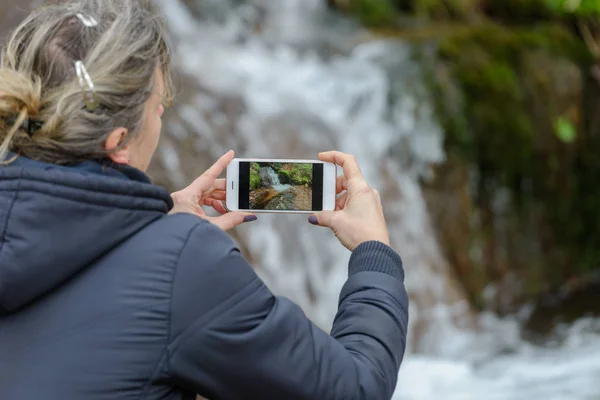 woman photographing a beautiful waterfall with a smartphone