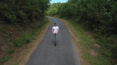 ormanda bir yolda elektrikli scooter sürme genç adam, yavaş hareket, drone çekim