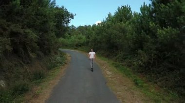 ormanda bir yolda elektrikli scooter sürme genç adam, yavaş hareket, drone çekim