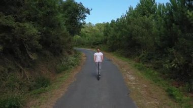 ormanda bir yolda elektrikli scooter sürme genç adam, yavaş hareket, drone çekim