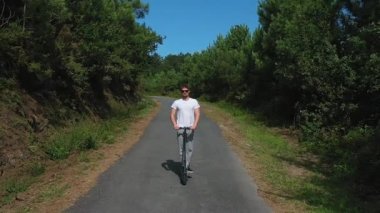 ormanda bir yolda elektrikli scooter sürme genç adam, yavaş hareket, drone çekim