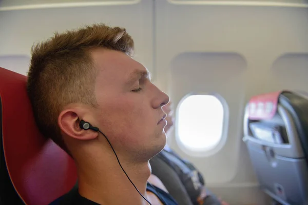 Joven con auriculares duerme en un asiento en un avión —  Fotos de Stock