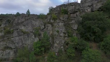 Emniyet halatına tırmanan biri uçuruma tırmanır. Kaya tırmanıcısı kayanın kenarlarına tutunur. İHA 'dan ateş ediliyor..