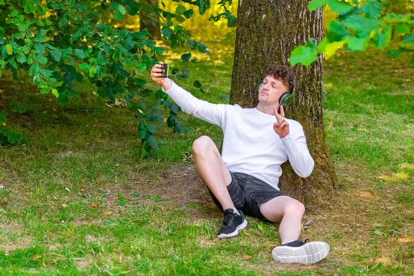 Jovem Homem Ruivo Fones Ouvido Sentado Inclinado Uma Árvore Tirando — Fotografia de Stock
