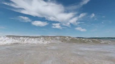 Dalgalar kıyıya vuruyor mavi gökyüzüne karşı, güneşli bir gün, yakın çekim düşük açılı, yavaş çekim