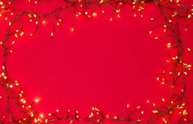 Kırmızı arka planda parlayan Noel teli ışıklarının manzarası. Şenlikli çelenk dekorasyonu, tatil tasarımı için mükemmel, Noel kartları. Noel ışıkları çerçevesi