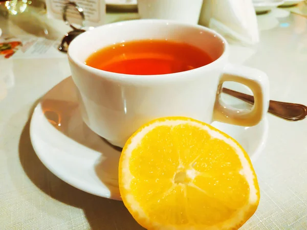 Xícara branca de chá preto com sabor quente com limão em um suporte branco . — Fotografia de Stock