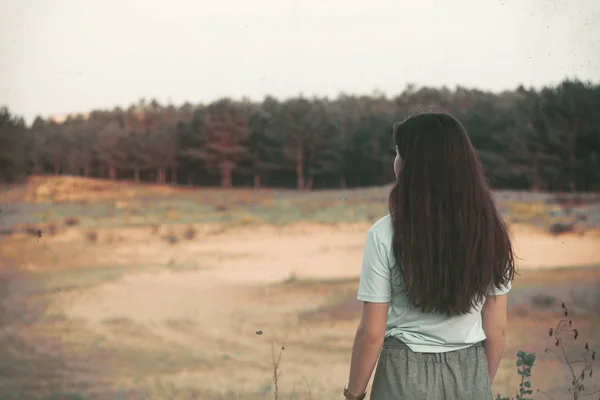 A girl with her back to the camera looks at nature. Long hair in a beautiful girl. — Stock Photo, Image