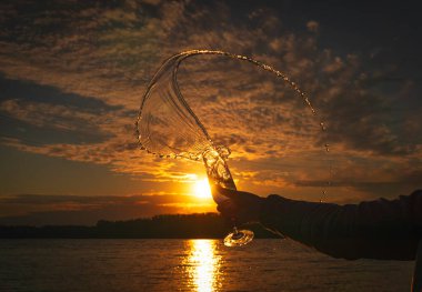 Güzel bir günbatımının arka planında bir bardak beyaz şarap, güneş ve gökyüzü alkolik bir içeceğe yansıyor. Tatil konsepti, otelde bir parti, doğada romantik bir akşam yemeği.