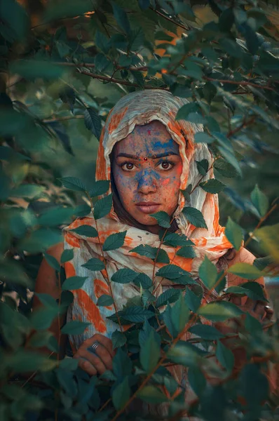 Young Indian faces in paint. A woman in traditional Indian dress celebrates Holi by color festival. A girl with black hair with a scarf on her head. Brown eyes oriental girls