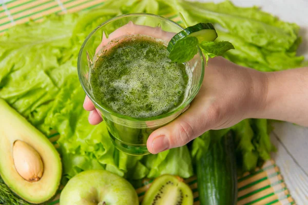 Hand hold healthy green smoothie against ingredients on wooden background