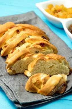 Tatlı örgülü ekmek parçası üzerinde mutfak havlu mavi ahşap zemin üzerine üzümlü.