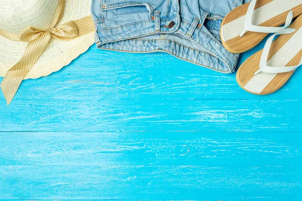 Πλαίσιο θηλυκό και κομψό καπέλο αχύρου παντόφλες τζιν σε μπλε φόντο ξύλινη, copyspace για το κείμενο, καλοκαιρινές διακοπές. — Φωτογραφία Αρχείου