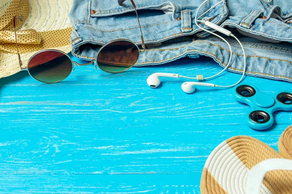 Πλαίσιο θηλυκό και κομψό καπέλο αχύρου παντόφλες τζιν γυαλιά ηλίου σε μπλε φόντο ξύλινη, copyspace για το κείμενο, καλοκαιρινές διακοπές. — Φωτογραφία Αρχείου