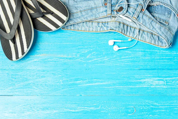 Πλαίσιο κομψό παντόφλες τζιν ακουστικά σε μπλε φόντο ξύλινη, copyspace για το κείμενο, καλοκαιρινές διακοπές. — Φωτογραφία Αρχείου
