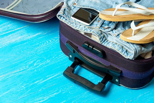 Maleta abierta con accesorios de viaje en mesa de madera azul con copyspace . — Foto de Stock
