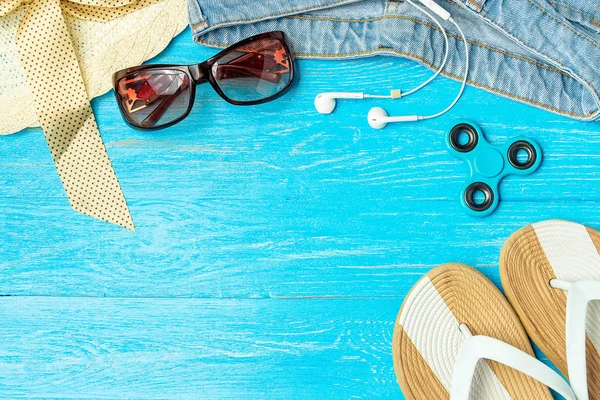 Marco elegante mujer sombrero de paja zapatillas jeans gafas de sol sobre fondo de madera azul, espacio de copia para el texto, vacaciones de verano . — Foto de Stock