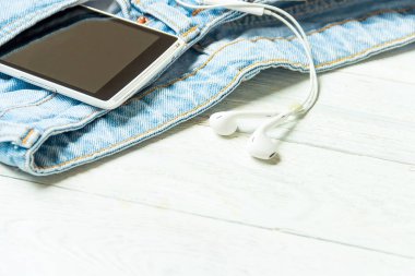 kulaklık ve smartphone cep eski kot boşaltmak Beyaz ahşap zemin üzerine vintage tarzı içinde.