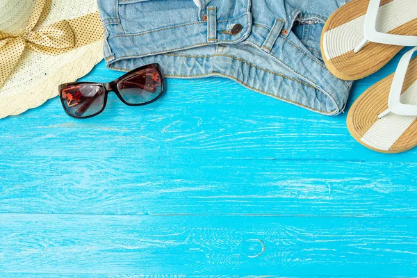 Marco elegante mujer sombrero de paja zapatillas jeans gafas de sol sobre fondo de madera azul, espacio de copia para el texto, vacaciones de verano . — Foto de Stock