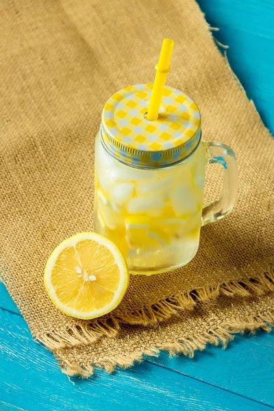 Acqua con limone. Limonata con fette di limone, vaso con paglia su fondo di legno blu . — Foto Stock